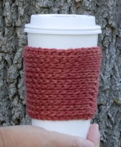 terracotta colored crochet yarn sleeve on a white disposable coffee cup.  tree bark background